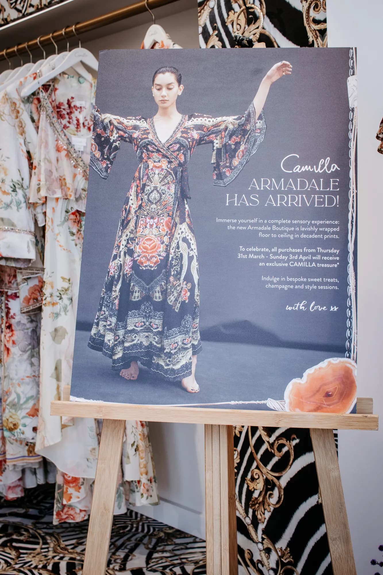 A store-opening poster on an easel among printed garments in the Camilla Armadale store