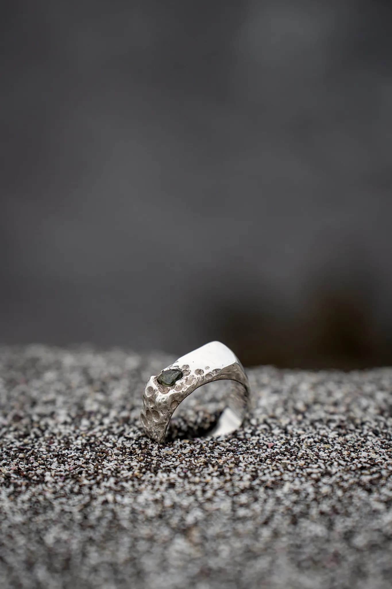 A silver ring on dark sand with a soft background