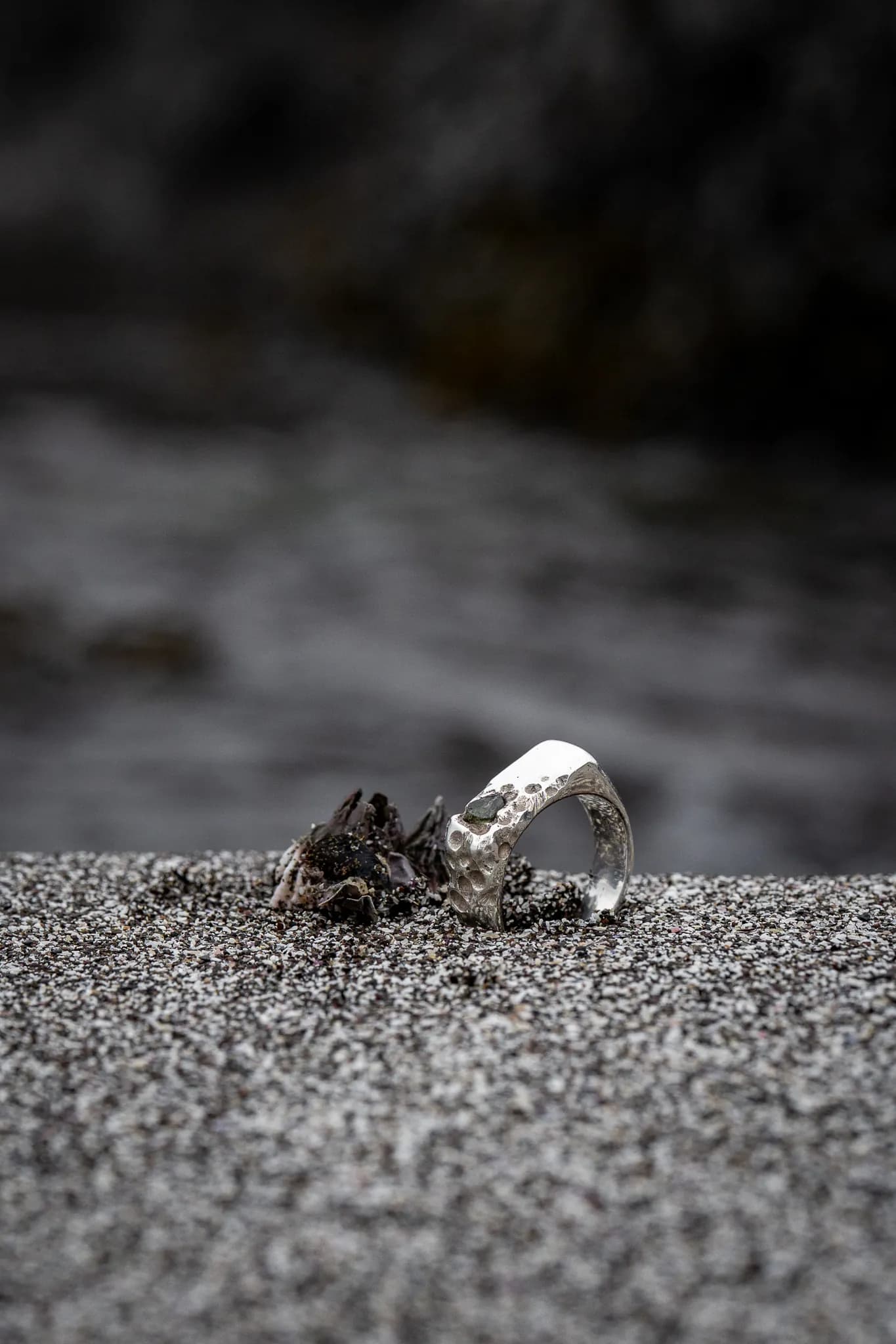 A silver ring set in dark sand, photographed close up