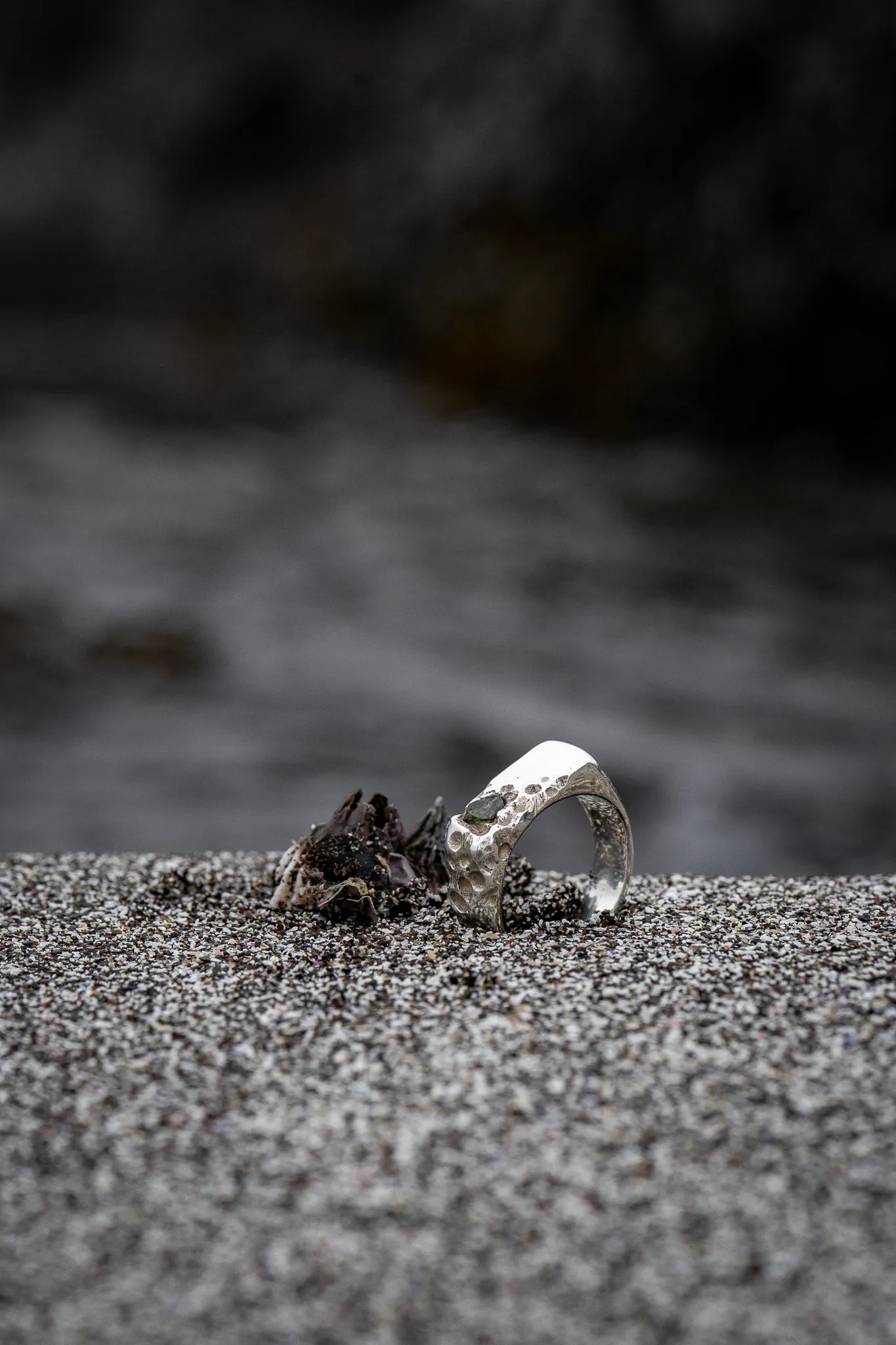 A silver ring set in dark sand, photographed close up
