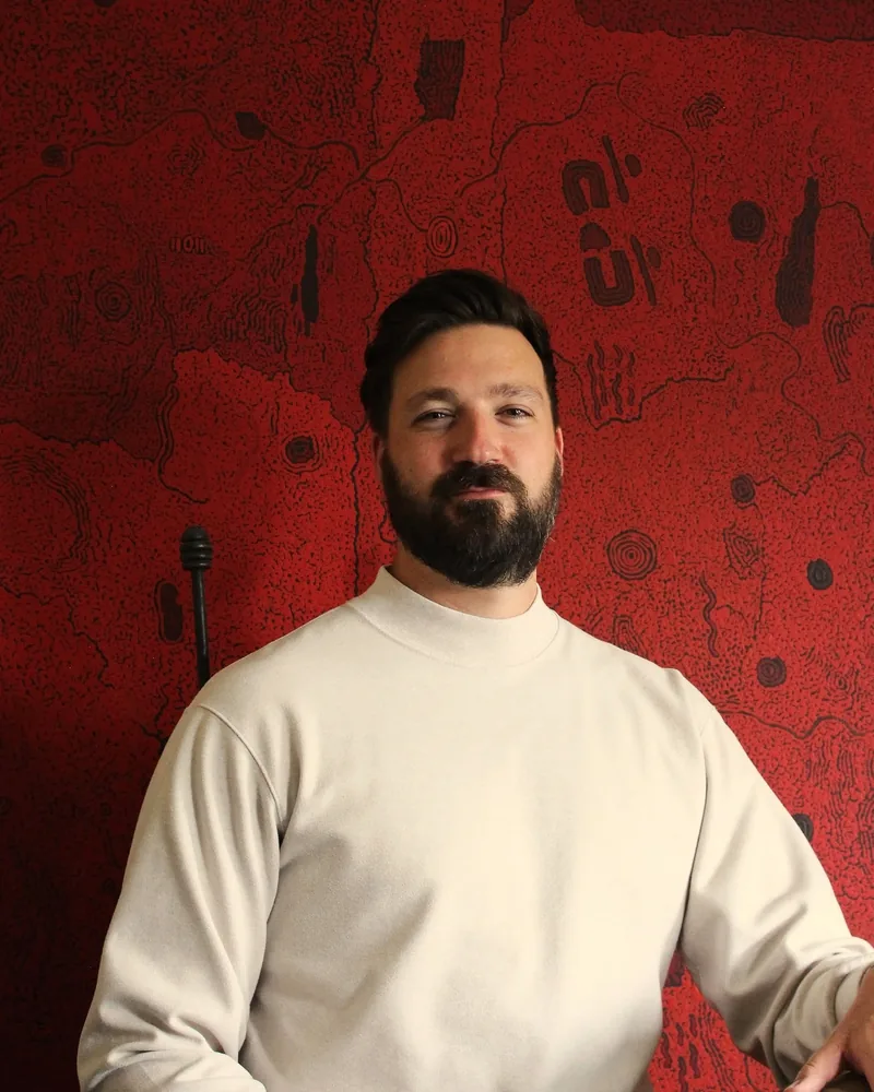 Sam Fossati, Design Director at FORJ, in front of a red dot painting