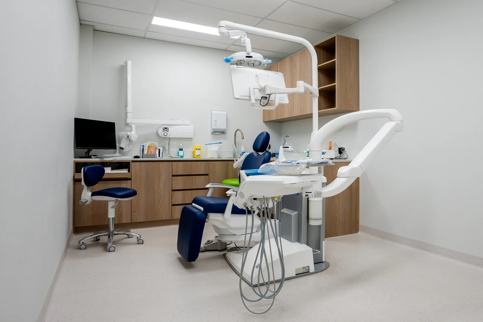 Dental treatment room with a blue chair, white cabinetry and timber-look joinery