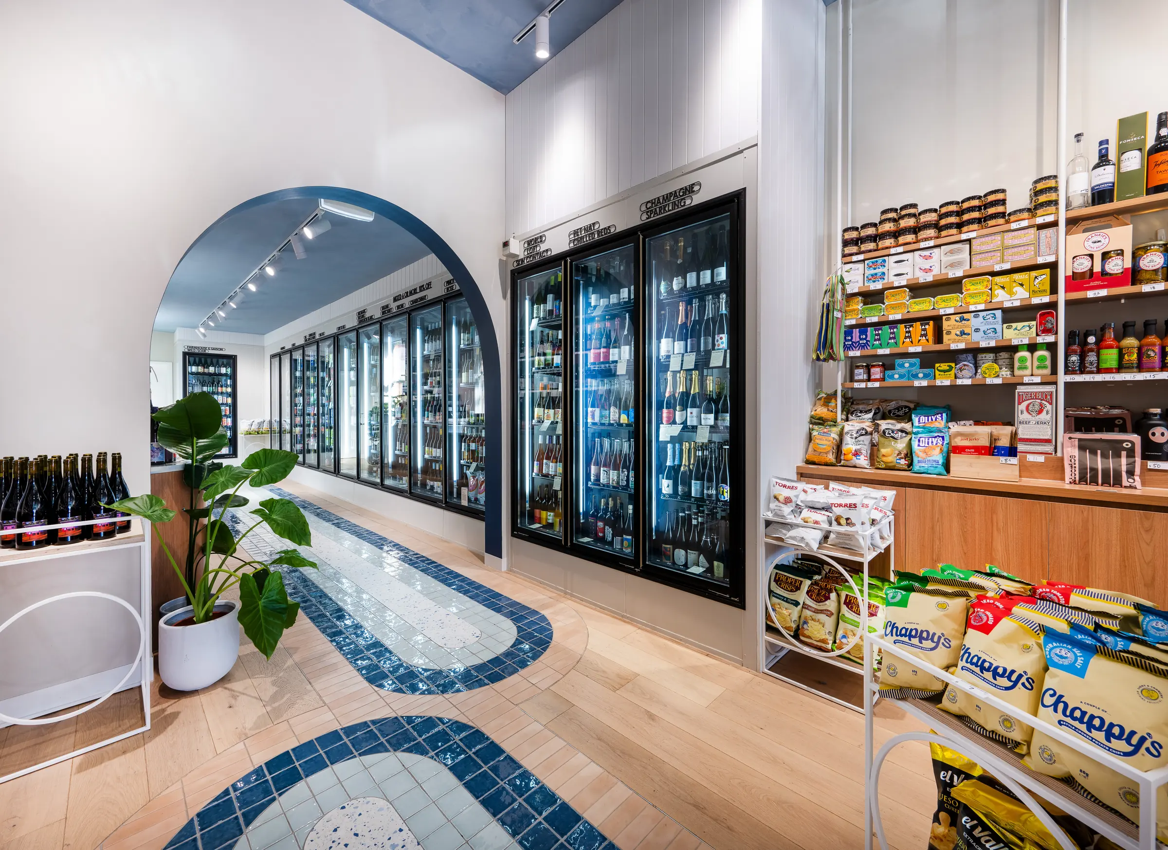 Blue arched opening at the rear of the store, with the tiled floor path curving past the fridges