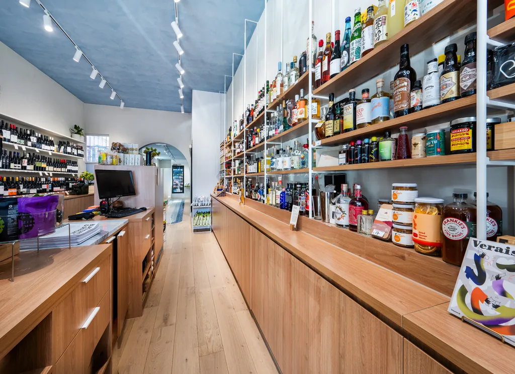 Long timber display counter under floor-to-ceiling shelving, the blue ceiling running back to the arched doorway