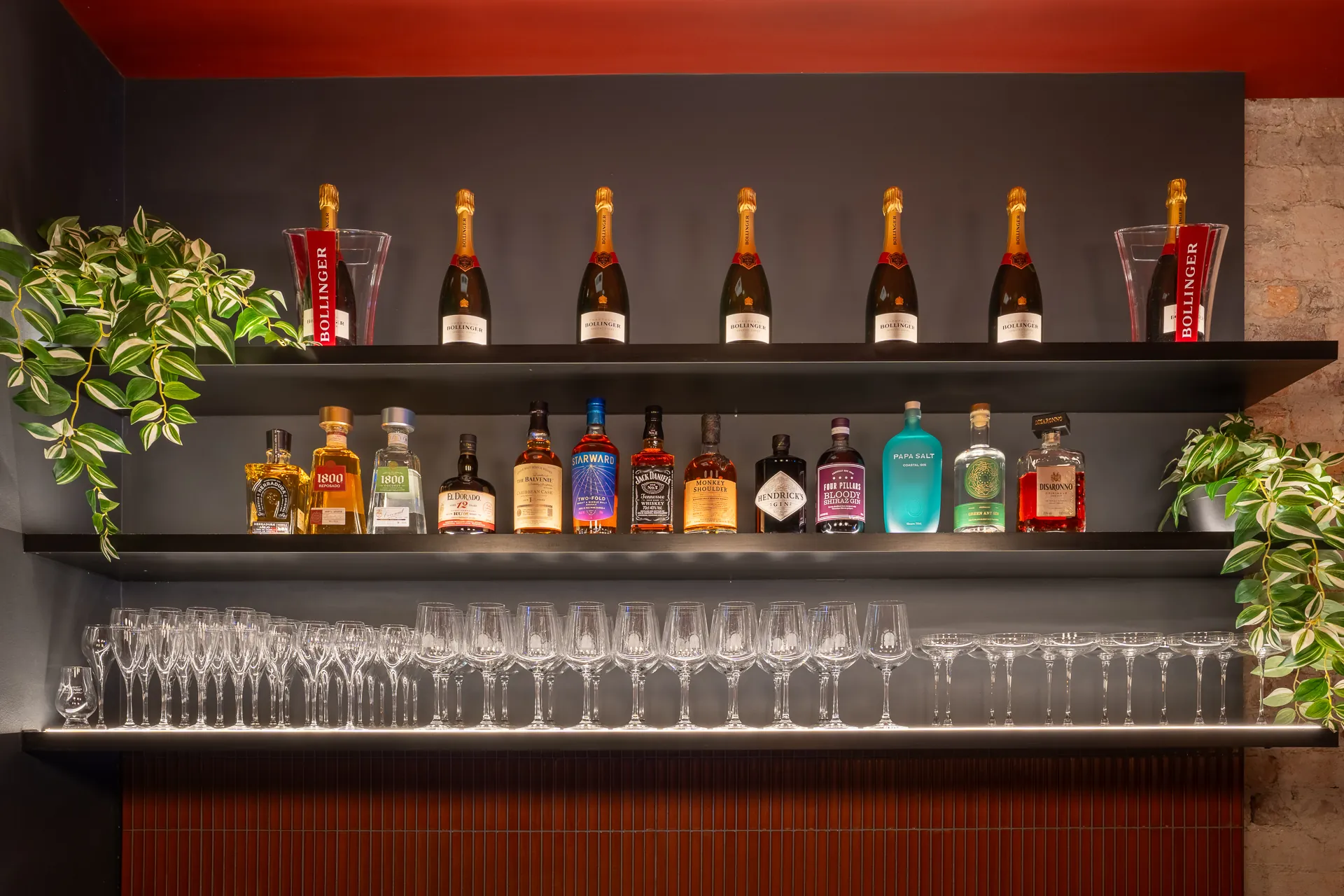 Back-bar shelving with bottles and glassware against a charcoal wall