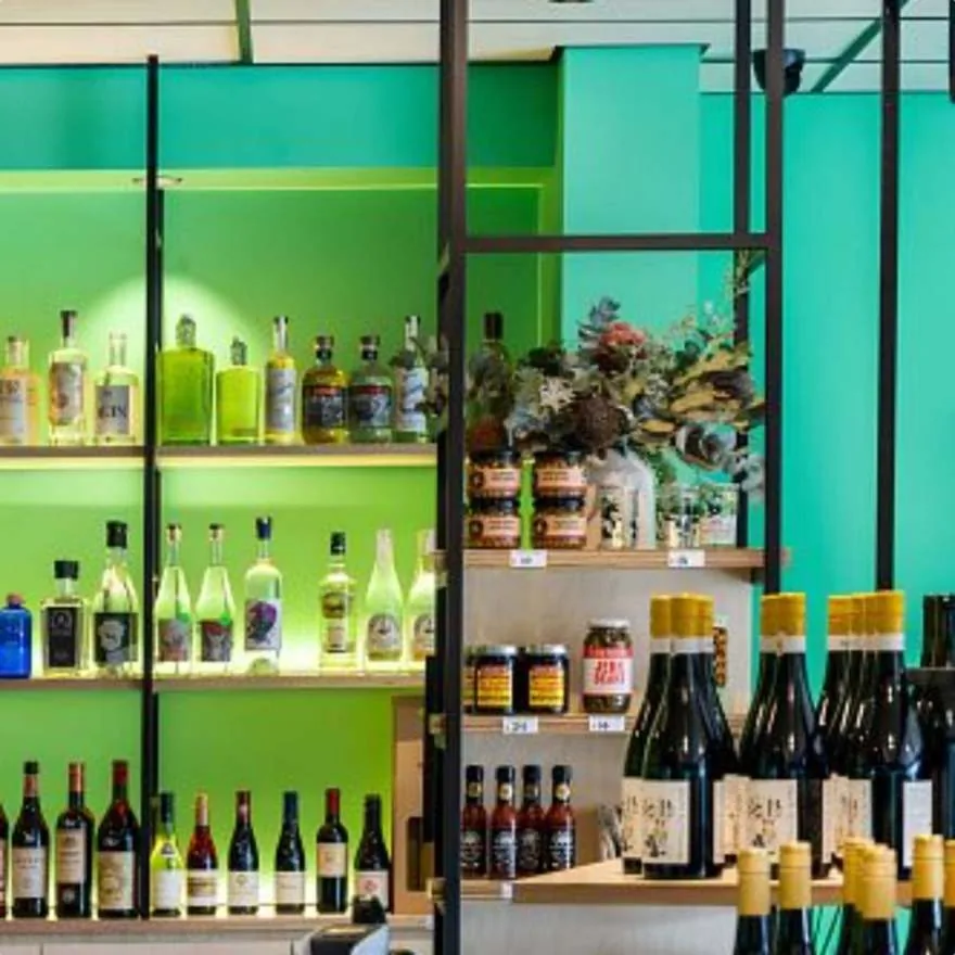 Wine and spirits on timber shelves against a green-lit wall, framed in black steel
