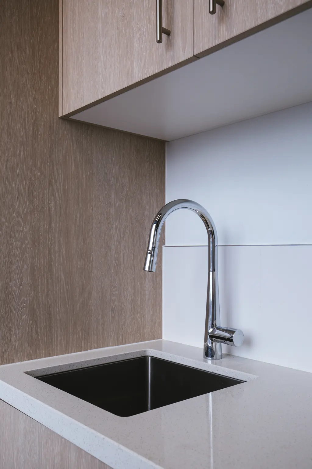 Kitchenette with timber-veneer cabinetry, stone benchtop and black sink