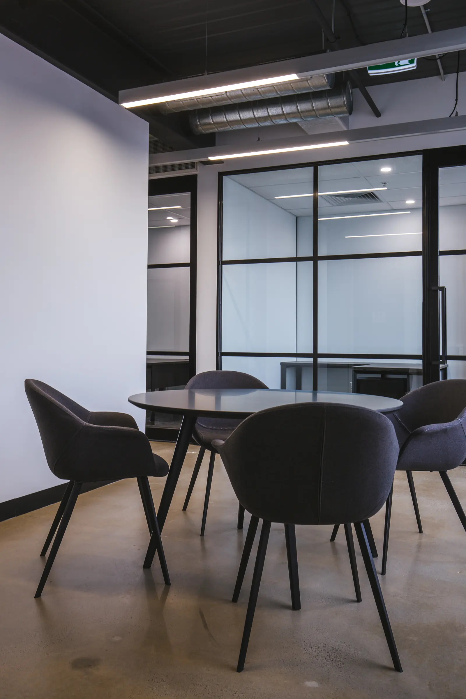 Round meeting table with upholstered chairs beside glazed partitions