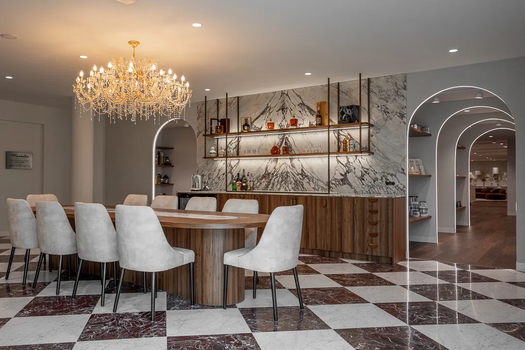 Meeting room with a long timber table, a veined marble wall with floating shelves, lit arched openings and a checkerboard marble floor