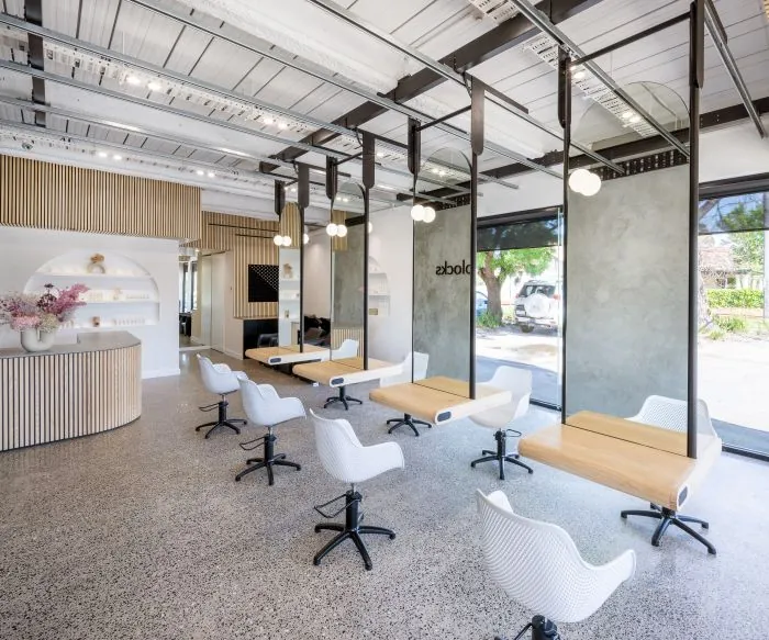 Salon floor with timber workstations, white chairs and black ceiling-mounted rails