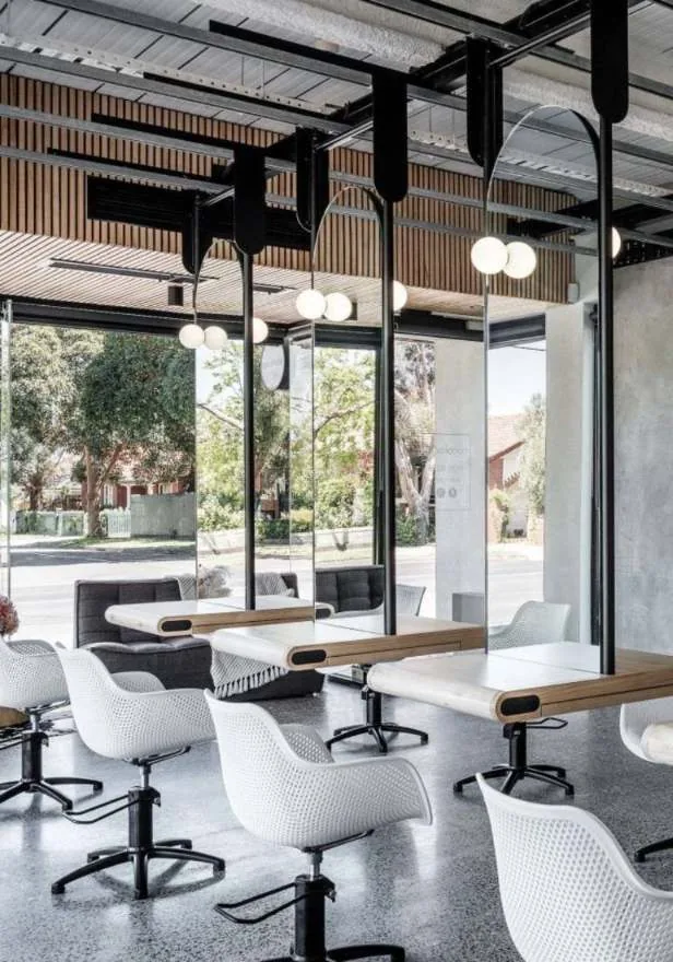 Salon stations in light timber with white chairs and black ceiling-mounted rails